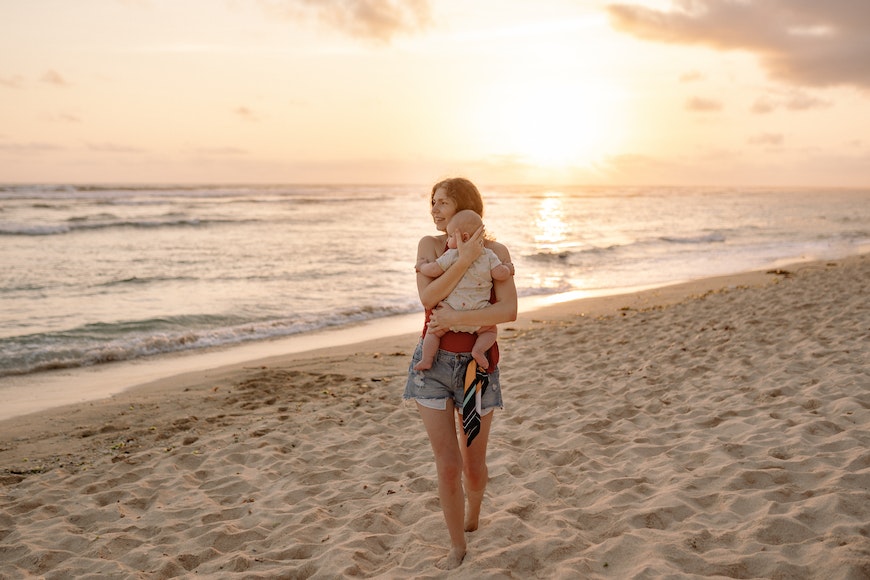 a woman standing on top of a sandy beach with a baby.
