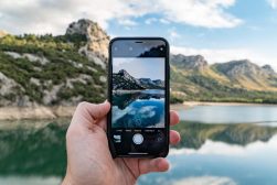 a person taking a picture of a mountain lake.