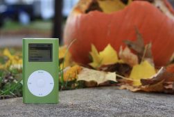 a green mp3 player sitting on top of a cement slab with a pumpkin in the background