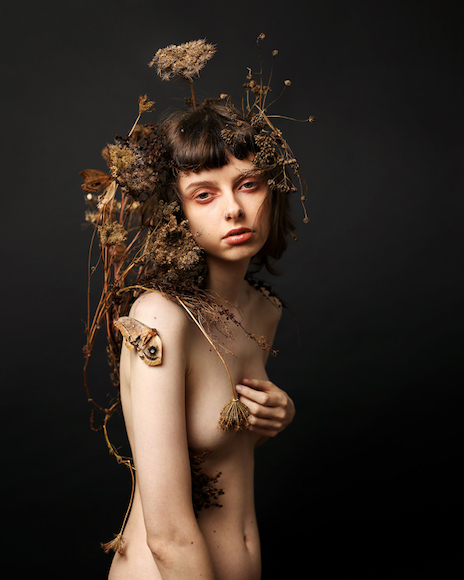 a nude woman posing with dried flowers on her head.
