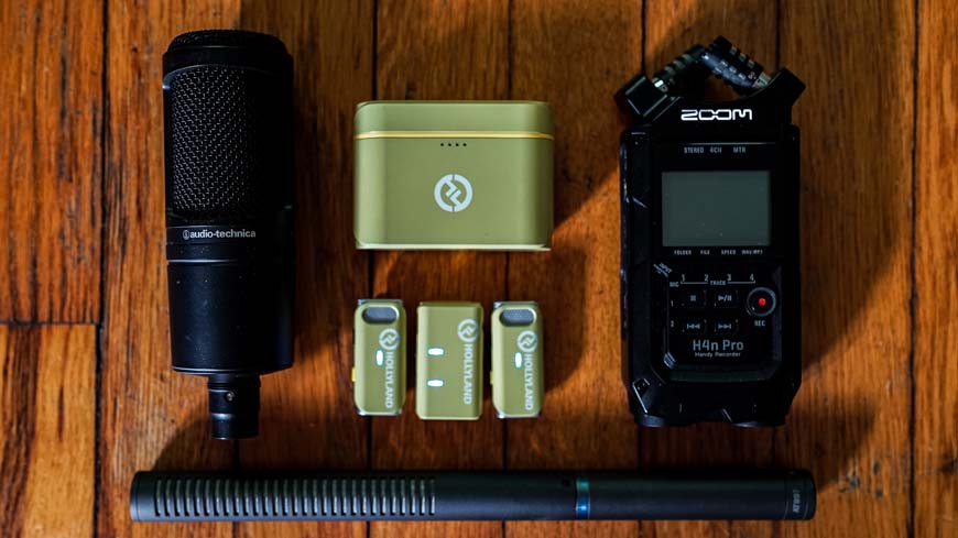 a lav mic, recorder, cardioid mic, and boom mic on a wooden table.