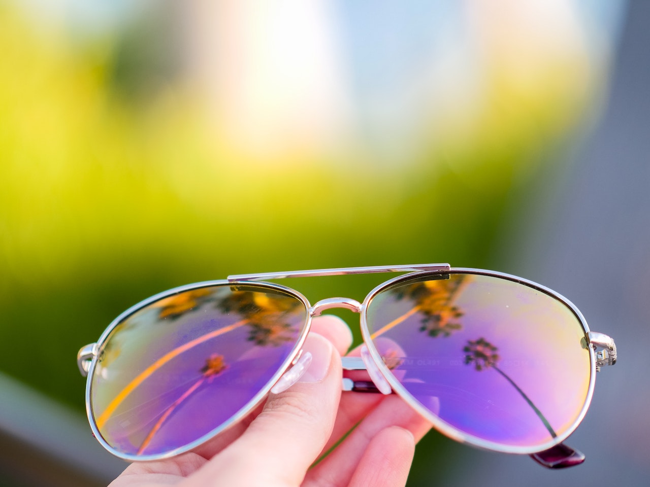 a person holding a pair of sunglasses with purple mirrored lenses.