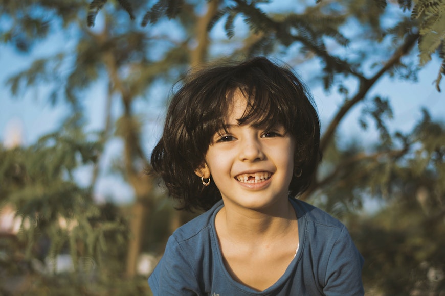 a young boy smiling in front of a tree.