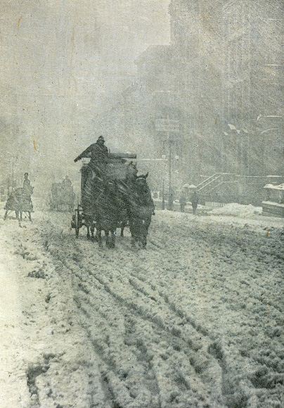 a horse drawn carriage driving down a snow covered street.