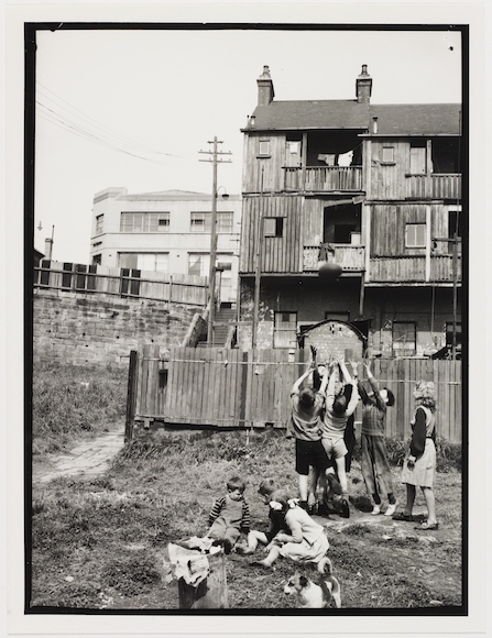 a black and white photo of a group of children in front of a house taken by Ted Hood.
