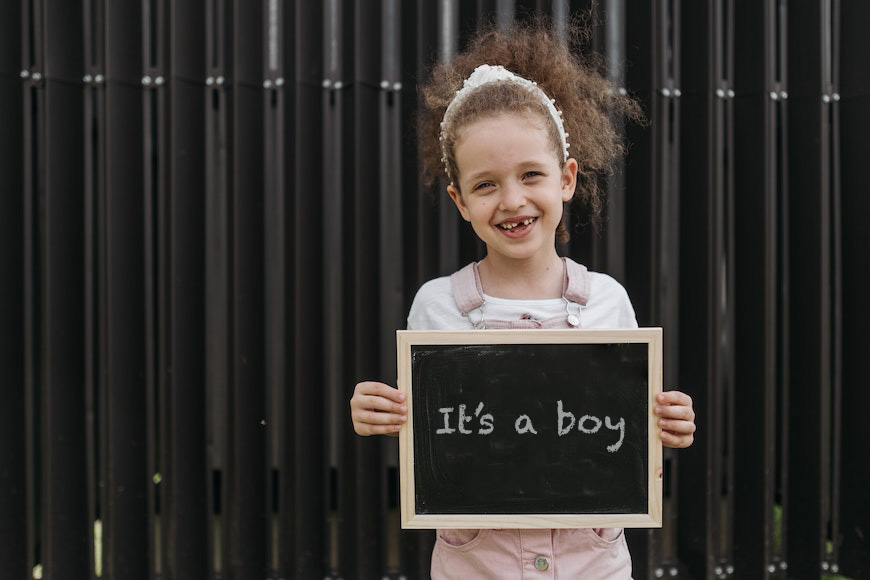 a little girl holding up a chalkboard that says it's a boy.