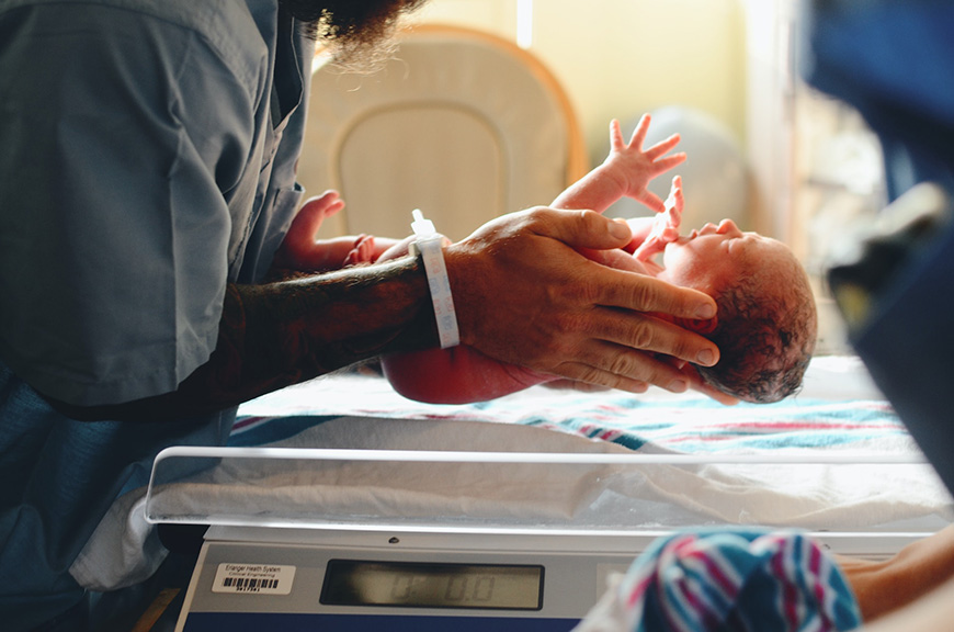 a person is weighing a baby in a hospital room.