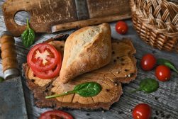 a slice of bread with tomatoes and basil on a wooden cutting board.