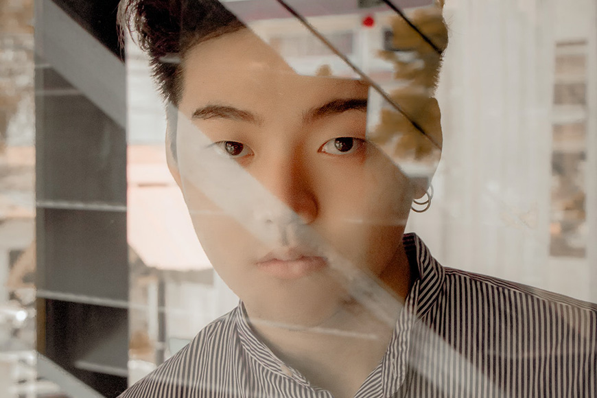 a young asian man looking out of a window.