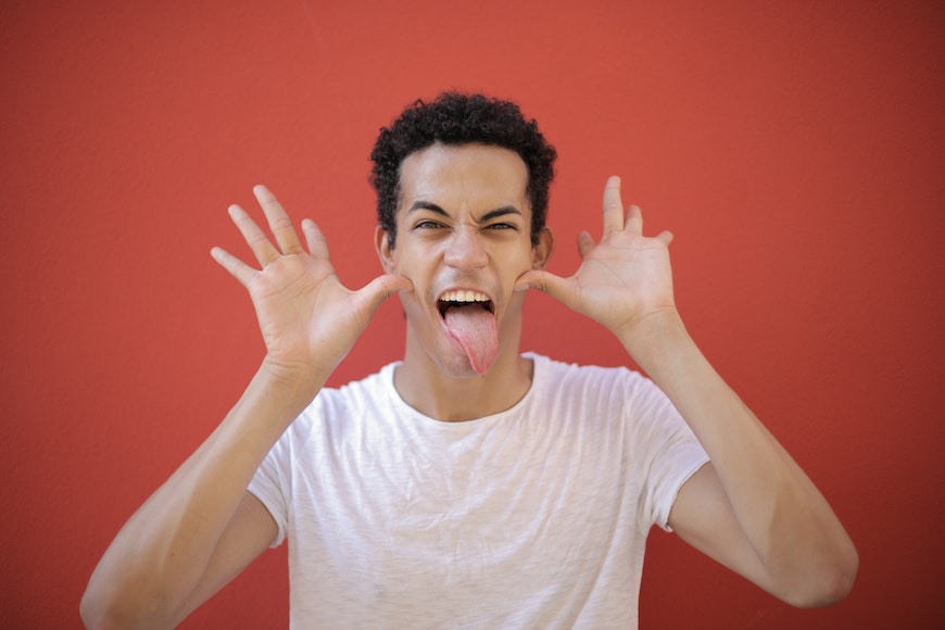 a young man with his tongue out on a red background.