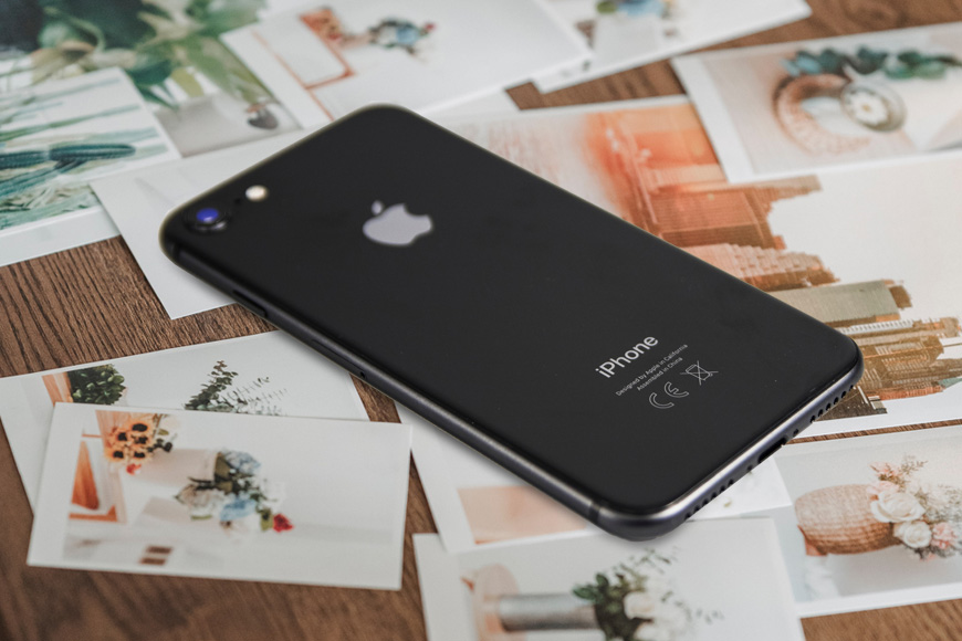 a black iphone is sitting on a table with photos on it.