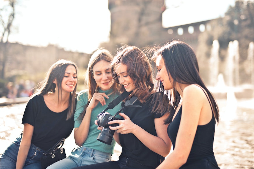 a group of young women looking at a camera in front of a fountain.