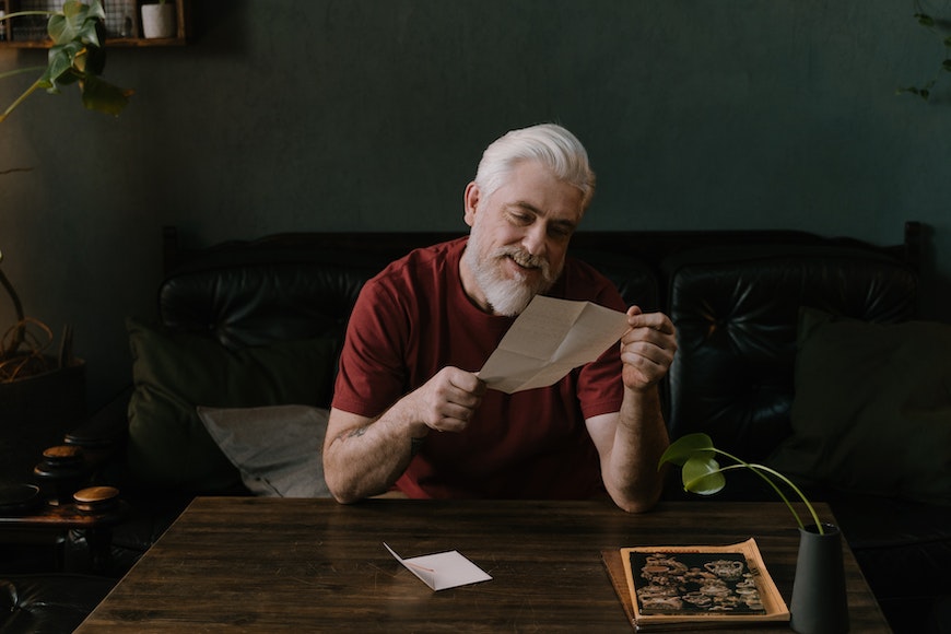 an elderly man is sitting at a table reading a letter.