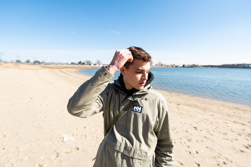 a young man standing on a beach with his hands on his head.