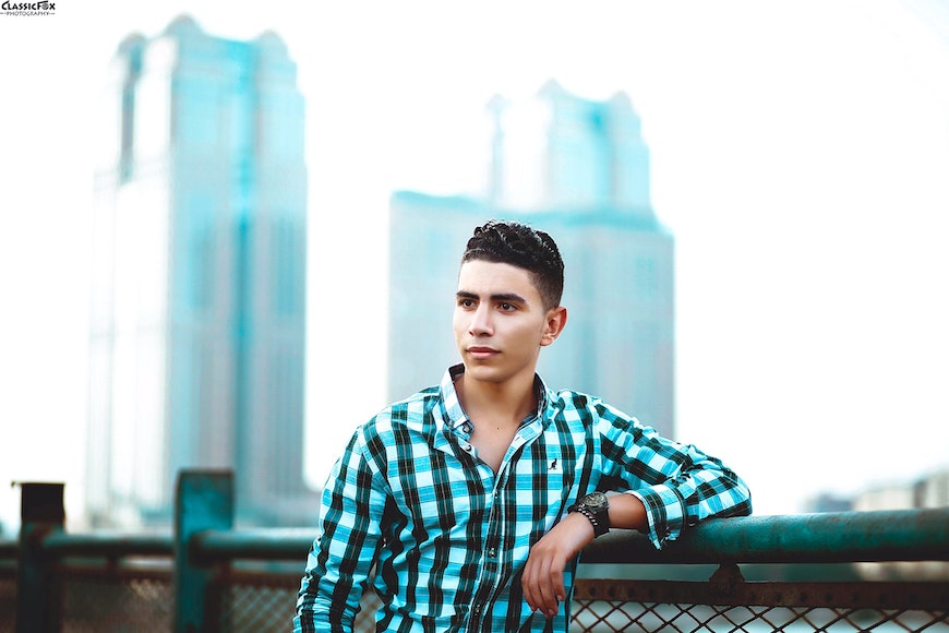 a young man in a plaid shirt leaning against a railing.