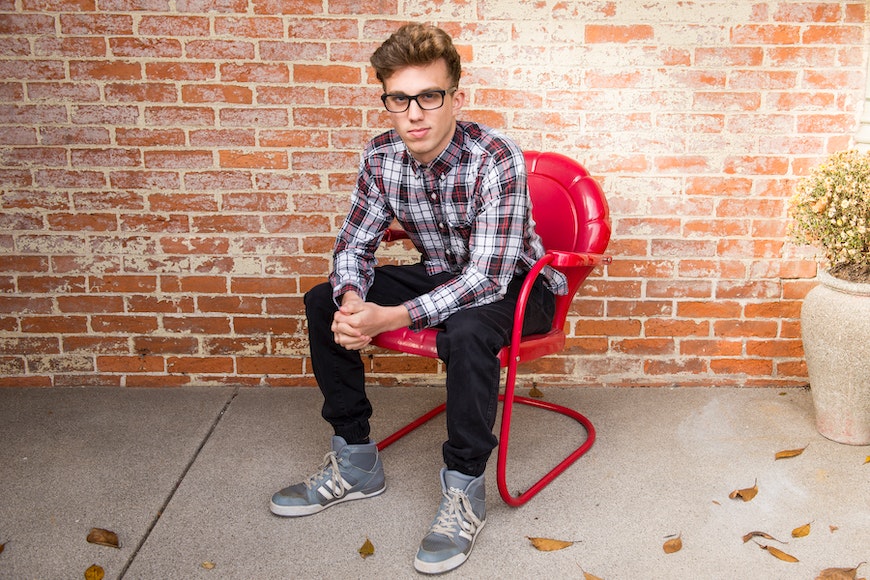 a young man sitting on a red chair in front of a brick wall.