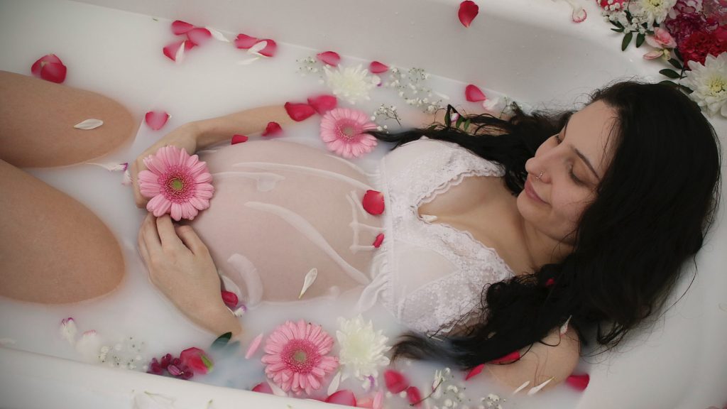 a pregnant woman laying in a bathtub with flowers.