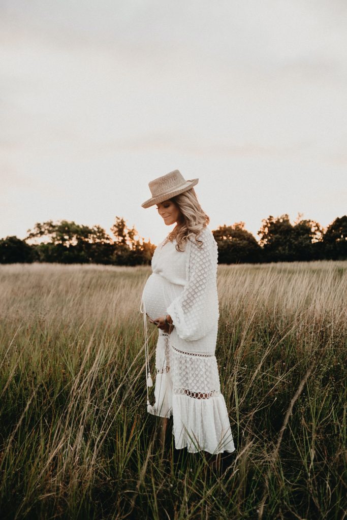 a pregnant woman in a white dress standing in a field at sunset.