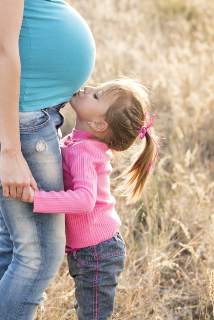 a pregnant woman kissing a little girl in a field.