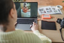 a woman is using a laptop with a hard drive and printed photos on the table
