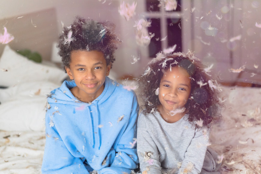 two children sitting on a bed with feathers flying around them.