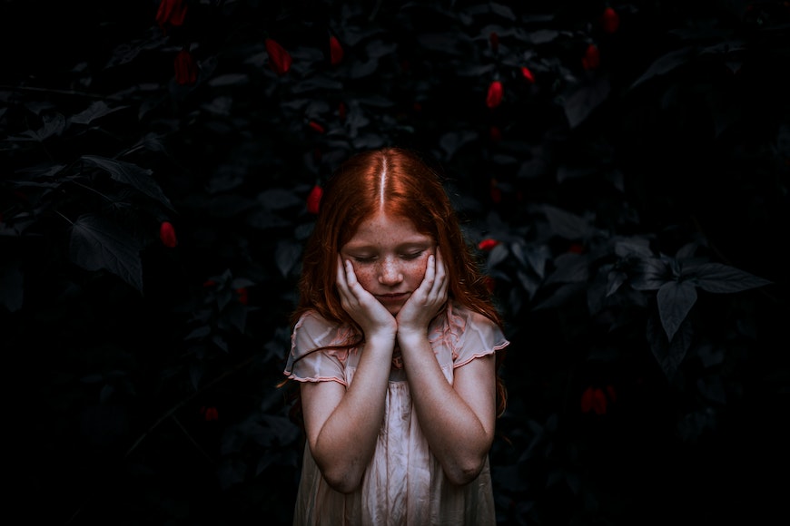 a girl with red hair is standing in the dark with her hands on her face.