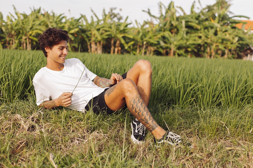 a man lying in grass with a tattoo on his leg.
