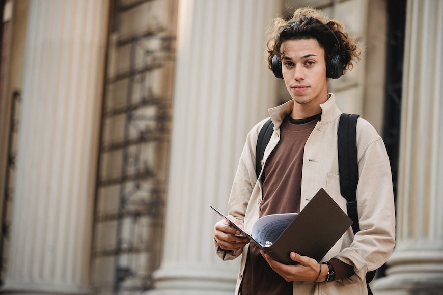 a young man wearing headphones and holding a book in front of a building.