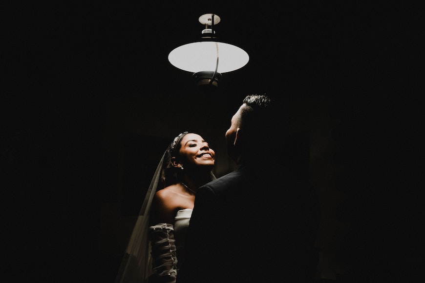 a bride and groom standing under a light in the dark.