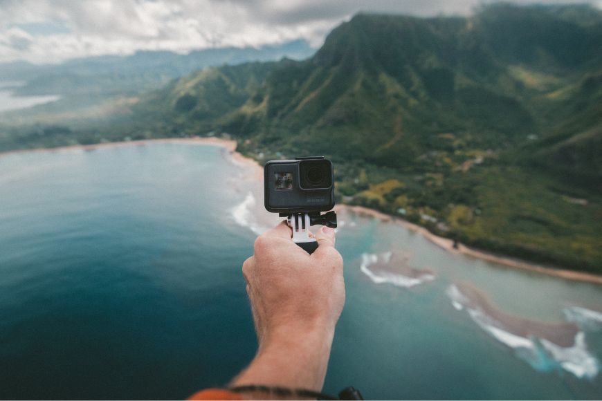 A person holding a gopro camera over the ocean.