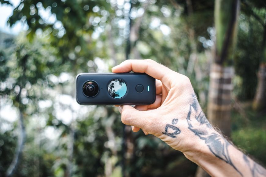 A person holding up Insta360 camera with tattoos on it.