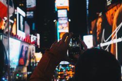 A person taking a photo in times square at night.