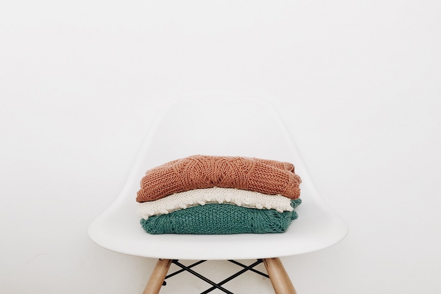 A stack of knitted sweaters on a white chair.