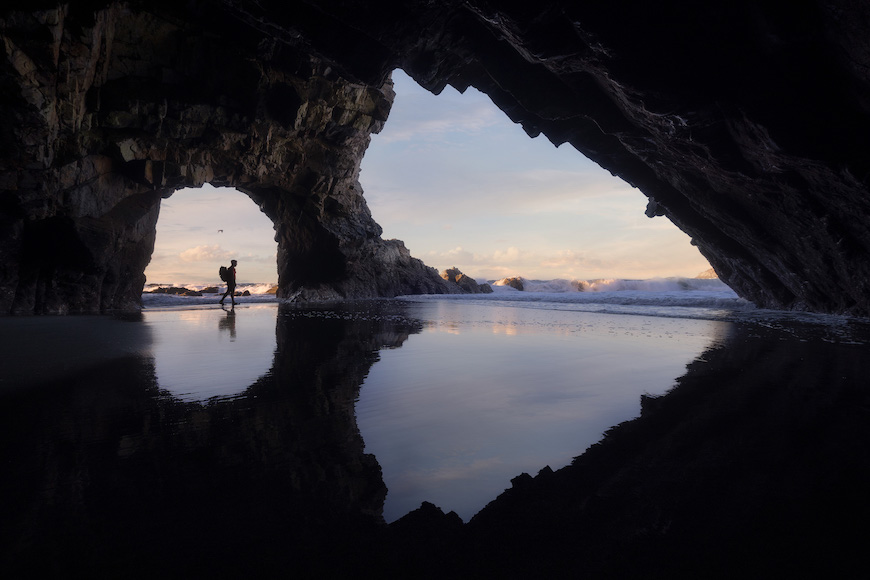A person standing inside a cave on the beach.