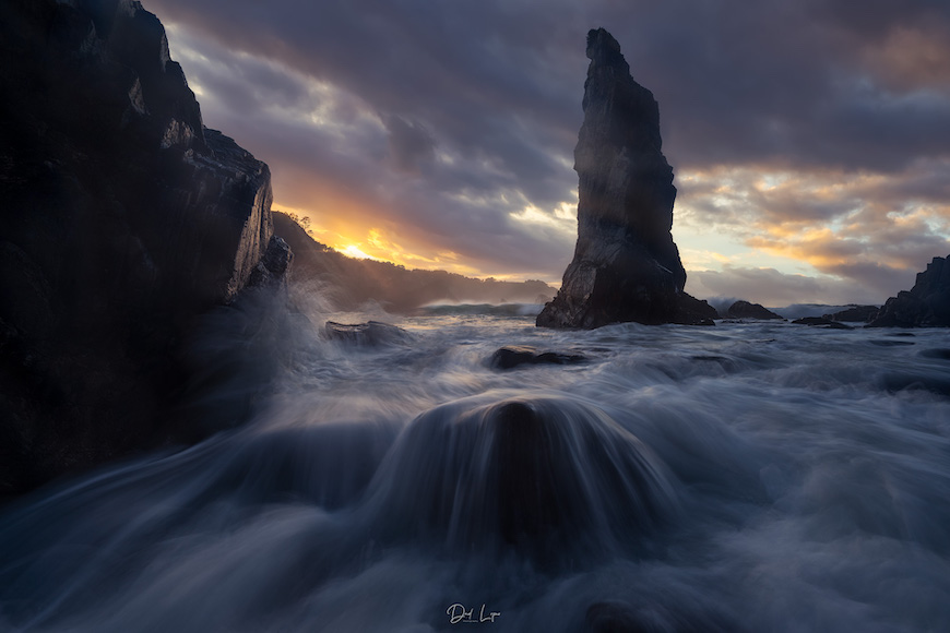 An image of a rock formation in the ocean at sunset.