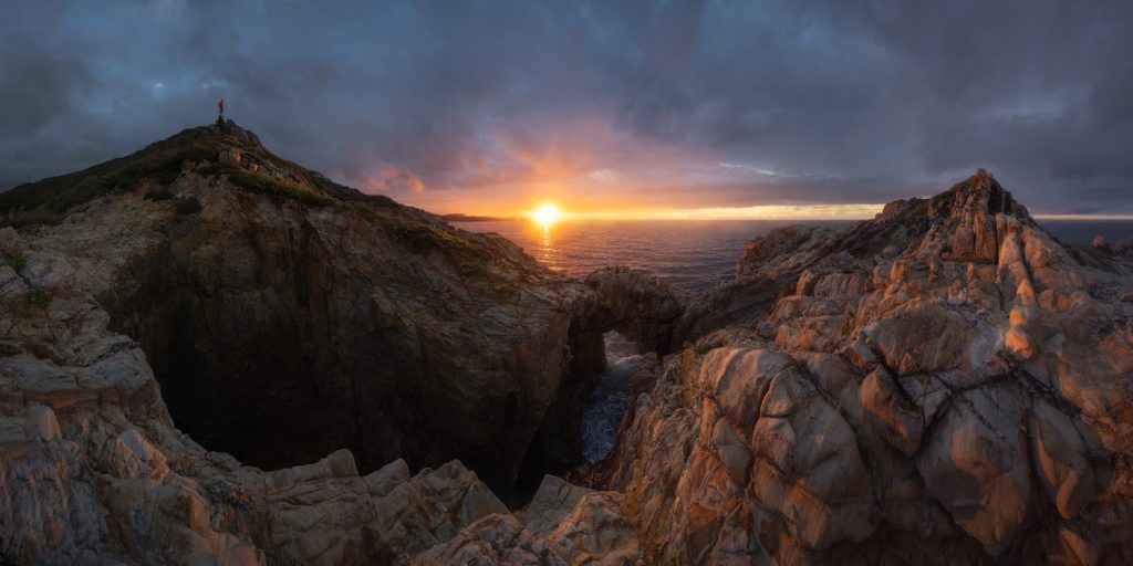 The sun is setting over a rocky cliff and ocean.