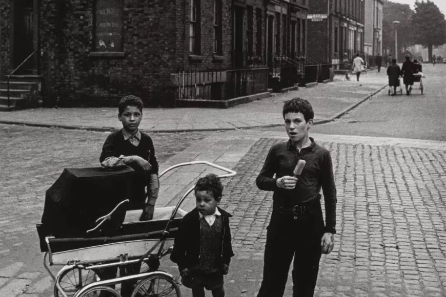 Two boys with a baby carriage on a cobbled street.