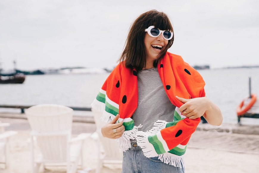 A woman wearing sunglasses and a watermelon scarf on the beach.