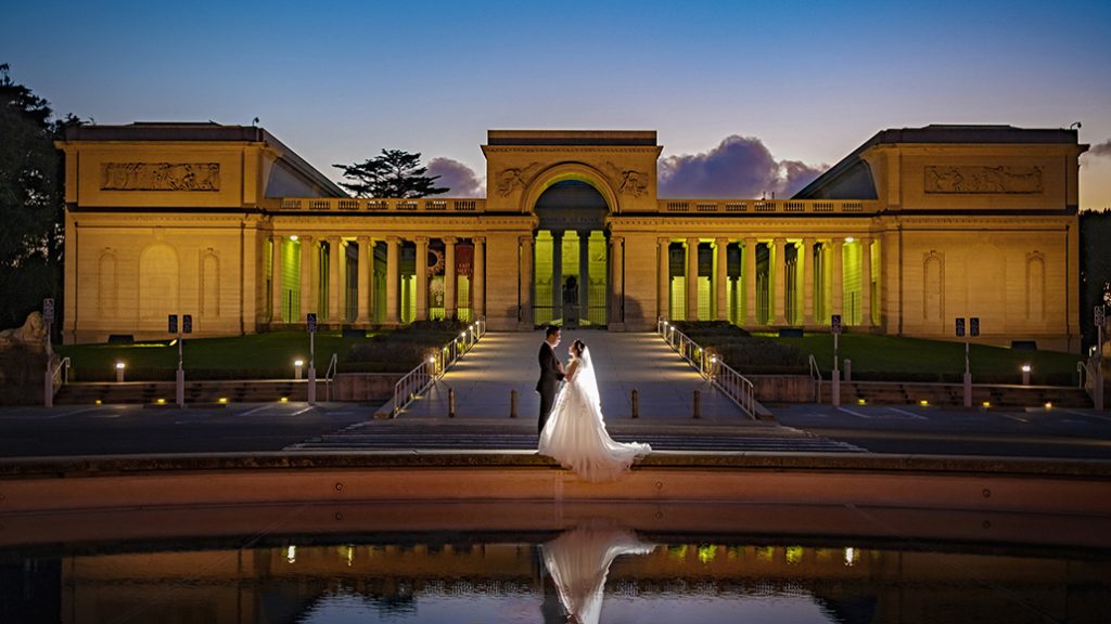 A bride and groom standing in front of a building at dusk.