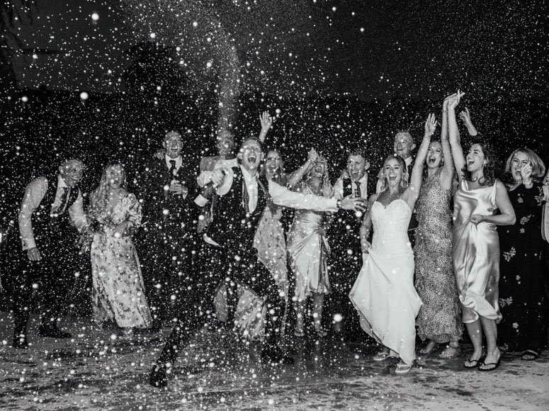 A black and white photo of a wedding party throwing snow at each other.