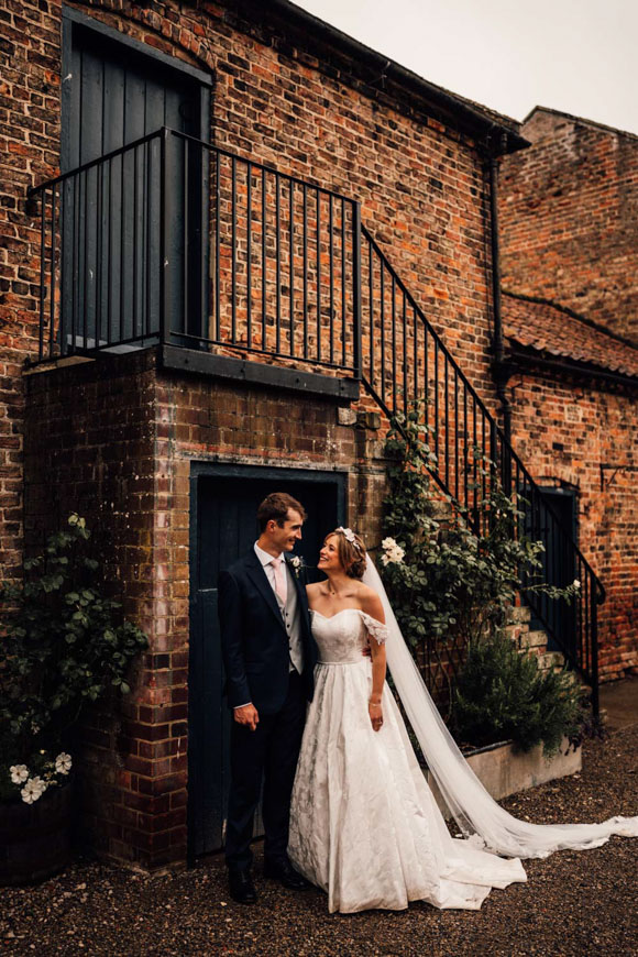 A bride and groom standing in front of a brick building.
