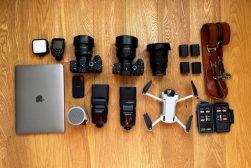 A laptop, camera, and other items are laid out on a wooden floor.