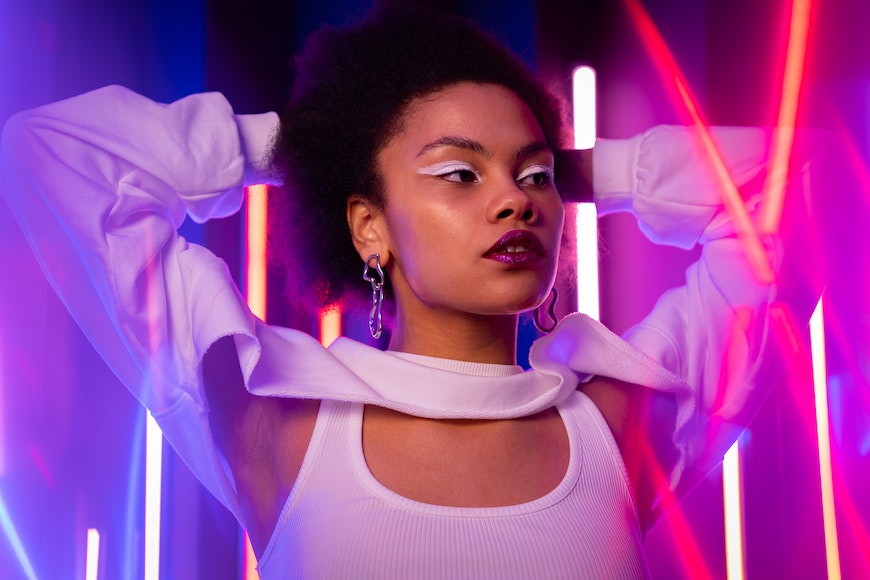 A woman with afro hair posing in front of neon lights.
