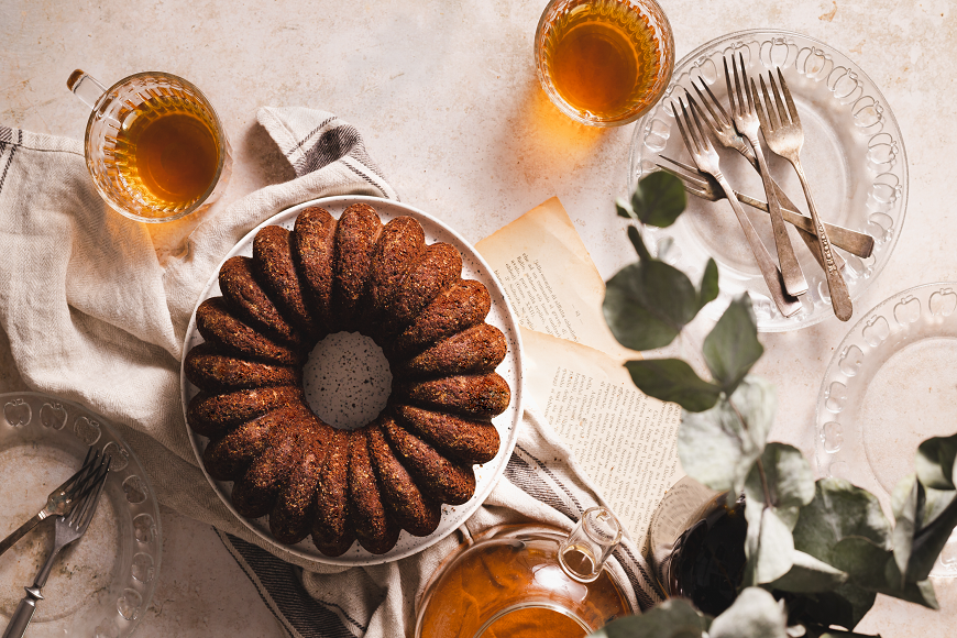 A bundt cake is sitting on a table next to a cup of tea.