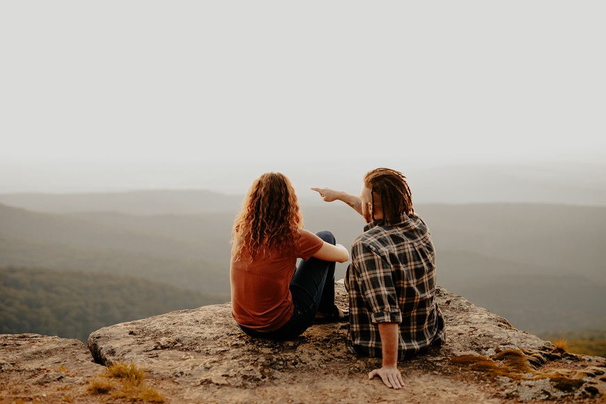 Two people sitting on top of a mountain overlooking a valley.
