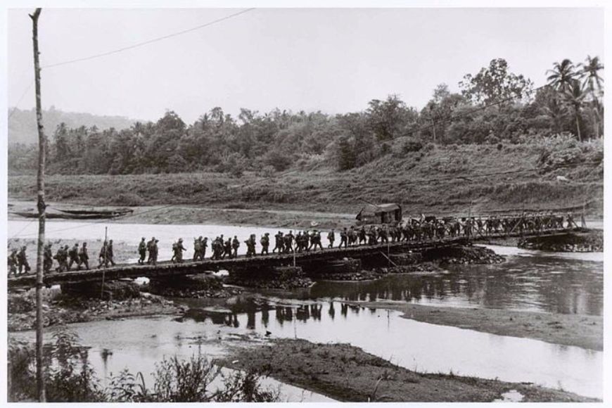A group of people crossing a bridge over a river.