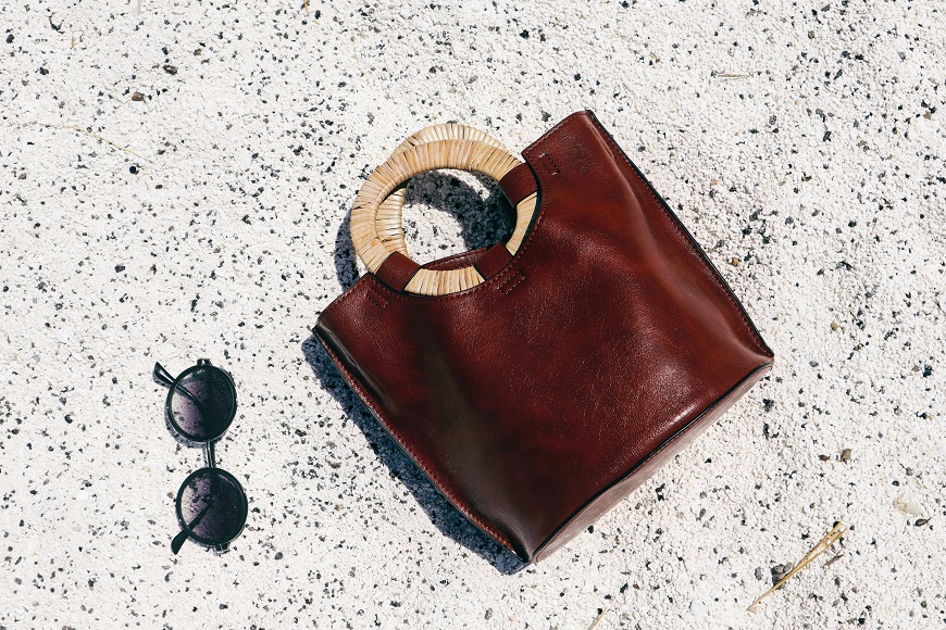 A brown leather tote bag with sunglasses and sunglasses on the sand.