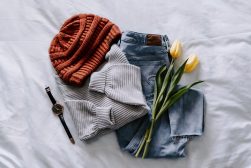 A pair of jeans, a beanie, a watch and tulips on a bed.