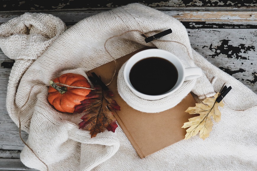 A cup of coffee and a pumpkin on a blanket.