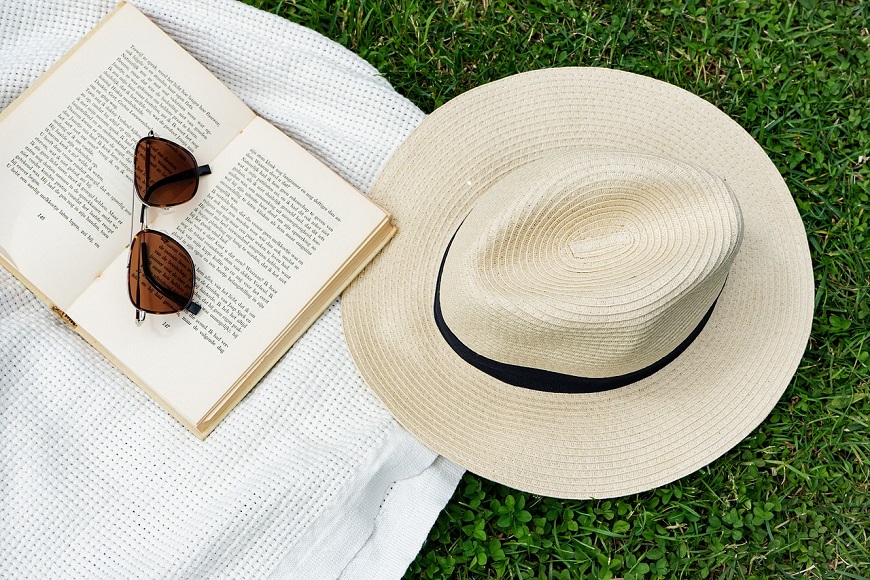 A hat, sunglasses and an open book on the grass.
